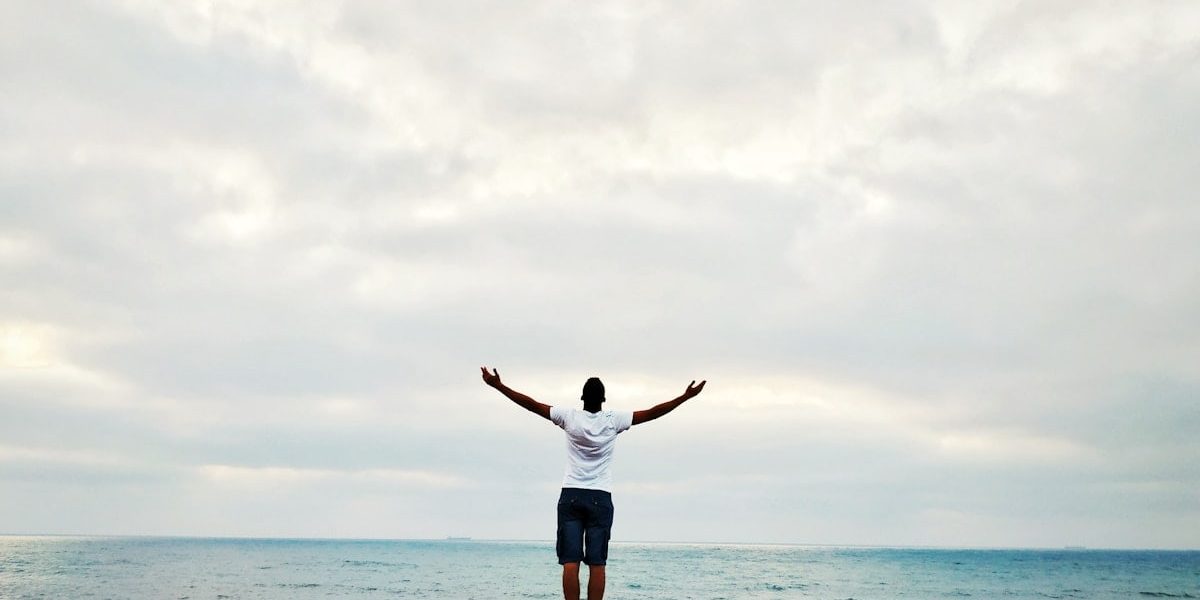 man raising hands standing near seashore during daytime