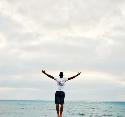 man raising hands standing near seashore during daytime