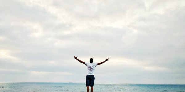 man raising hands standing near seashore during daytime