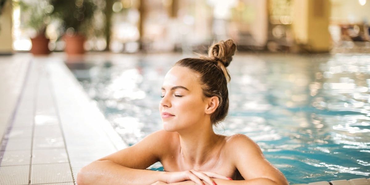 A serene woman relaxing on the edge of an indoor swimming pool, enjoying leisure time.